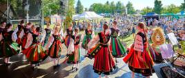 Szerokie ujęcie ze sceny na tańczący zespół folklorystyczny oraz licznie zgromadzoną na świeżym powietrzu publiczność.