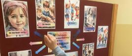 Uczeń i uczennica ubrani na niebiesko stoją przed gazetką tematyczną związaną z prawami dziecka, wskazują palcami na zdjęcia