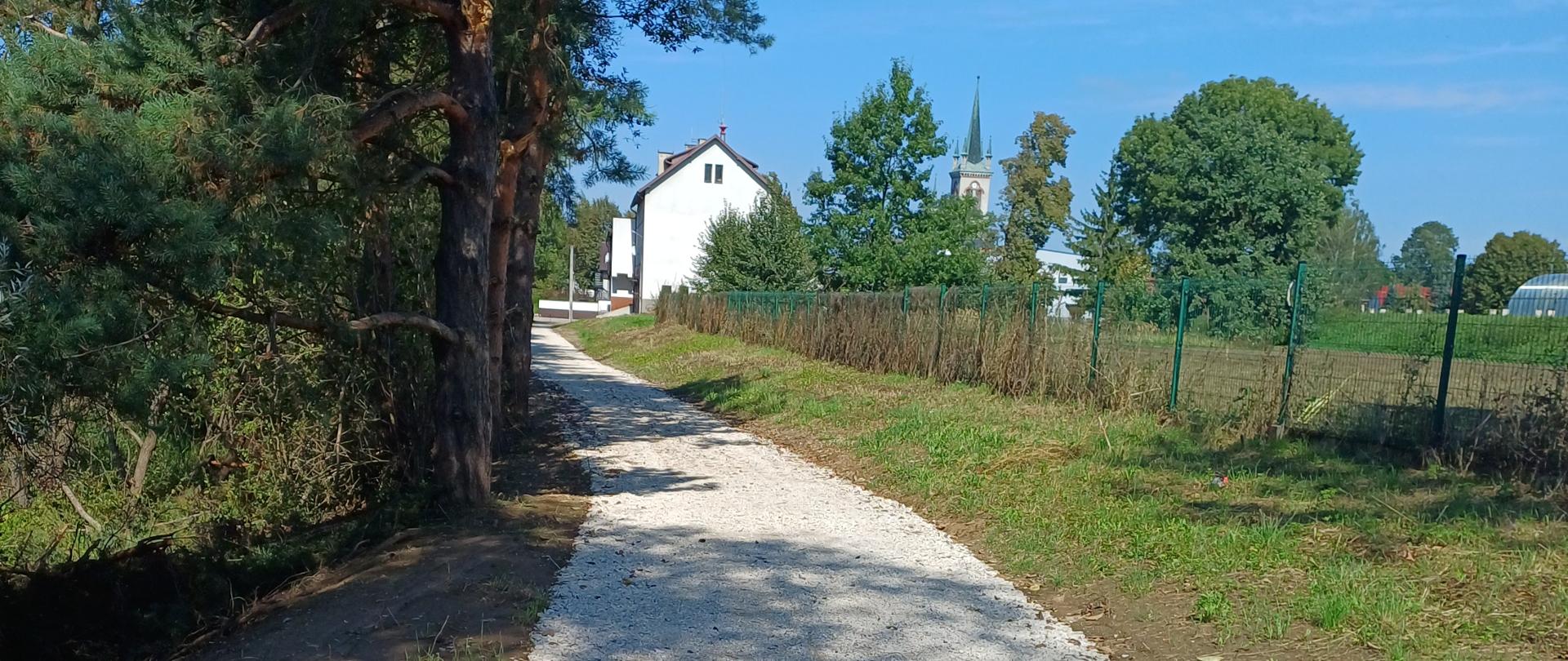 Żwirowa ścieżka prowadząca w stronę białego domu i kościoła w tle