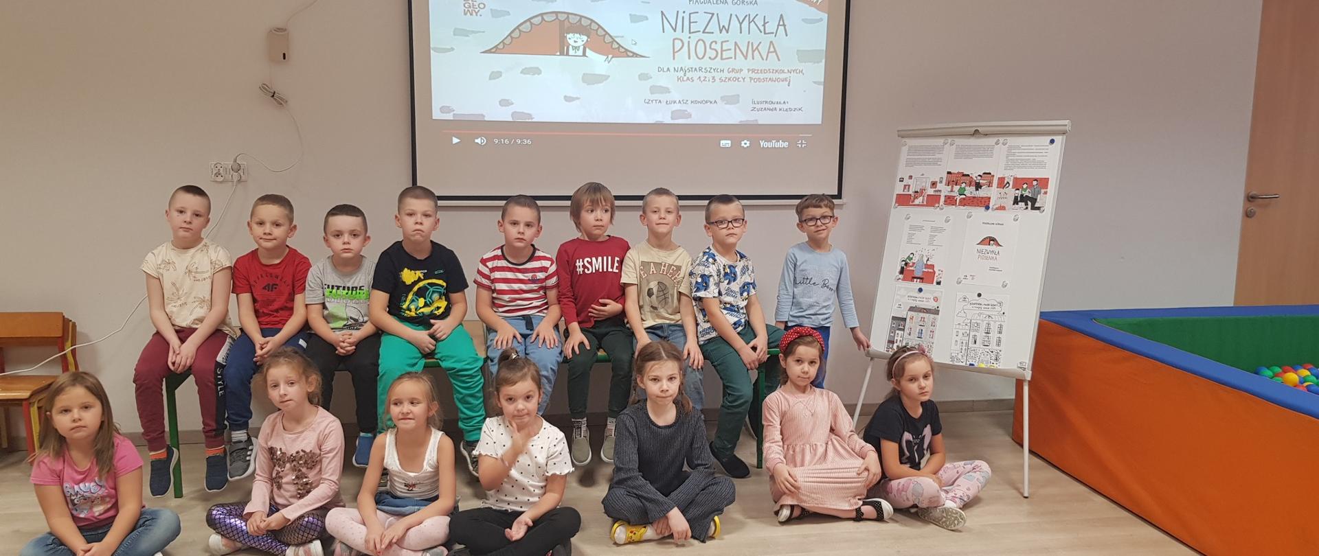 Grupa dzieci przed tablicą multimedialną i gazetką 
