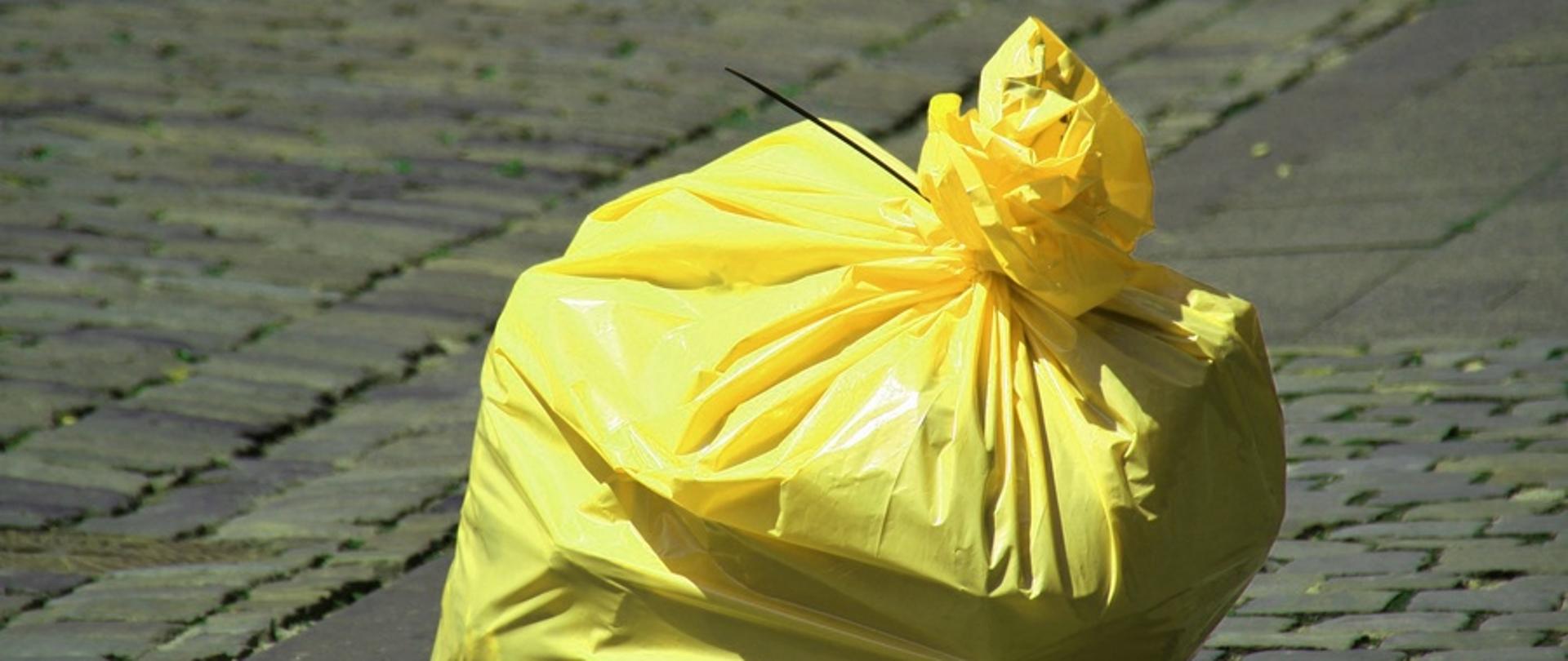 Żółty worek z odpadami zawiązany opaską zaciskową, pozostawiony na wybrukowanej nawierzchni