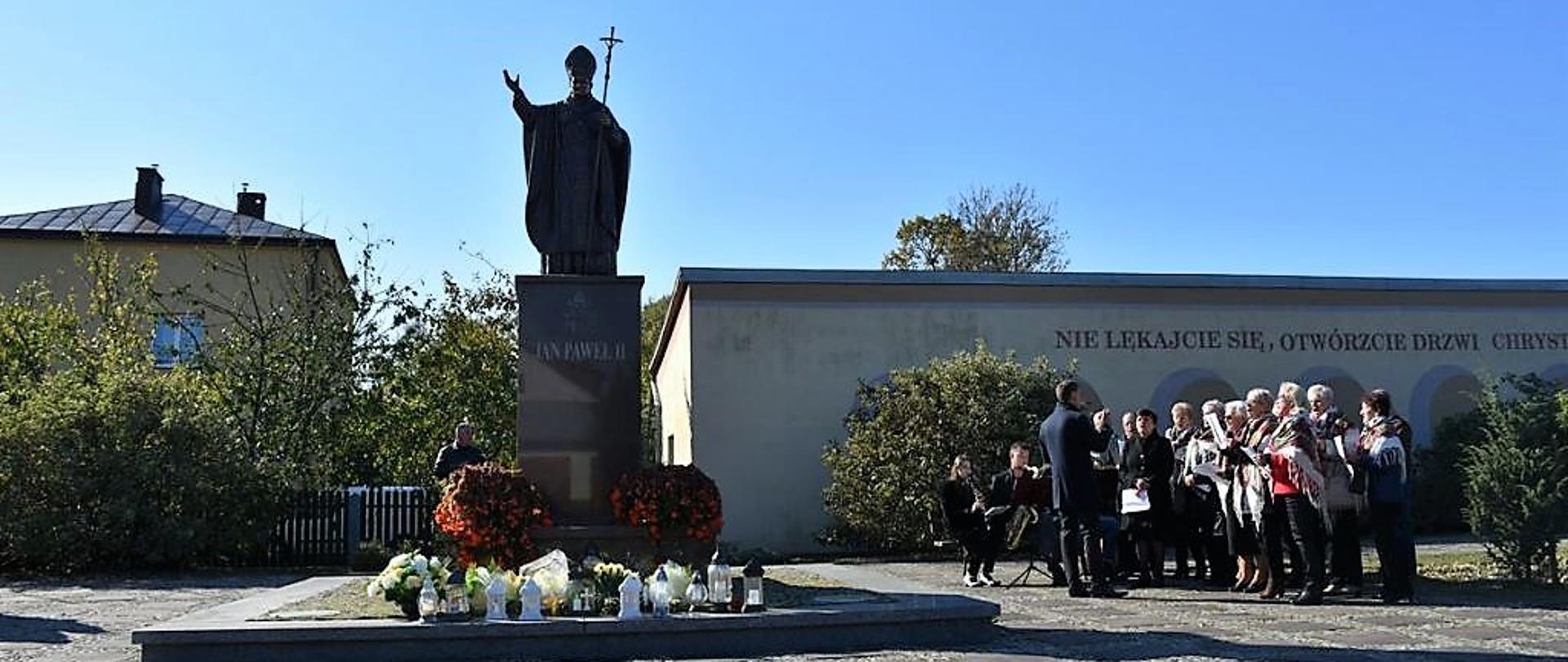 Pomnik Św. Jana Pawła II, po jego prawej stronie chór i orkiestra.