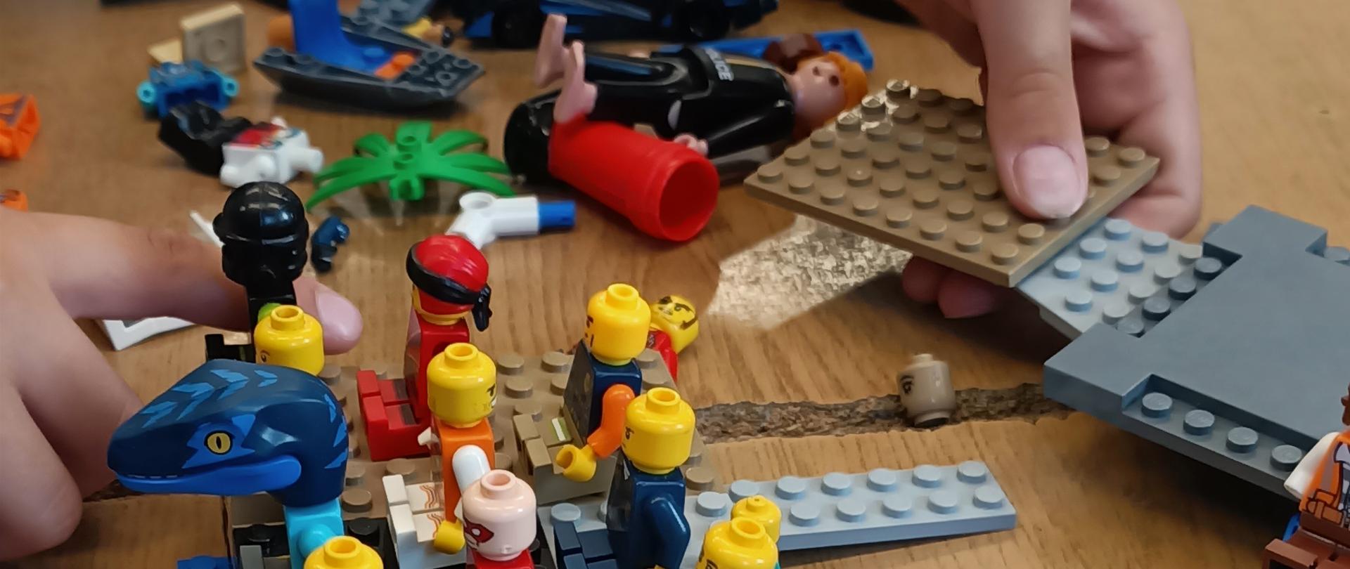 Na blacie stołu rozsypane klocki lego. Uczeń buduje model platformy z ludzikami.