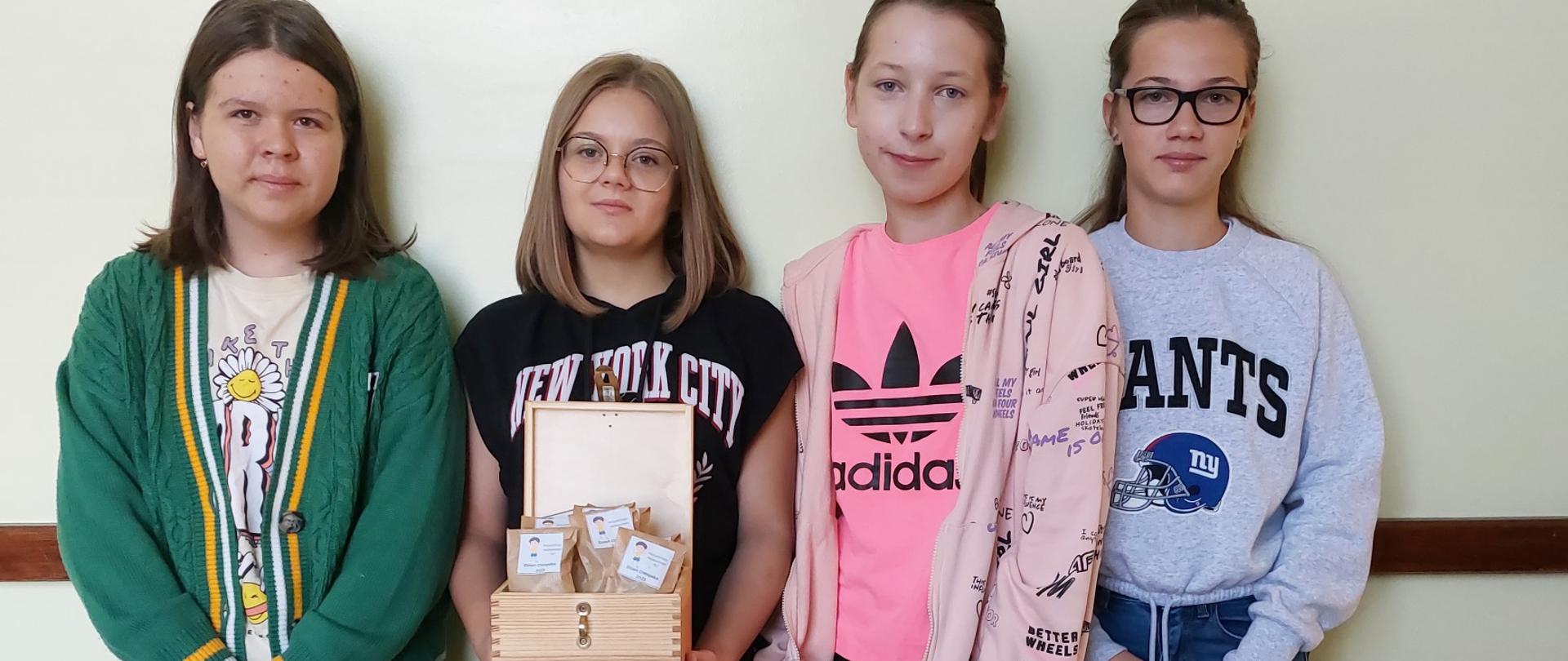 Uczennice klas starszych stoją na korytarzu szkolnym ze skrzynką z prezencikami dla kolegów.