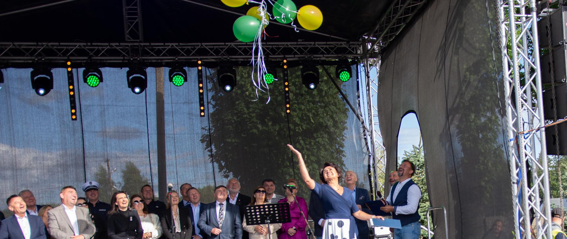 1. Zdj. przedstawia uroczyste powitanie i otwarcie festynu na scenie przez P. Wójt – Jolantę Orman. Na scenie widoczni przybyli goście reprezentujący instytucje samorządowe.