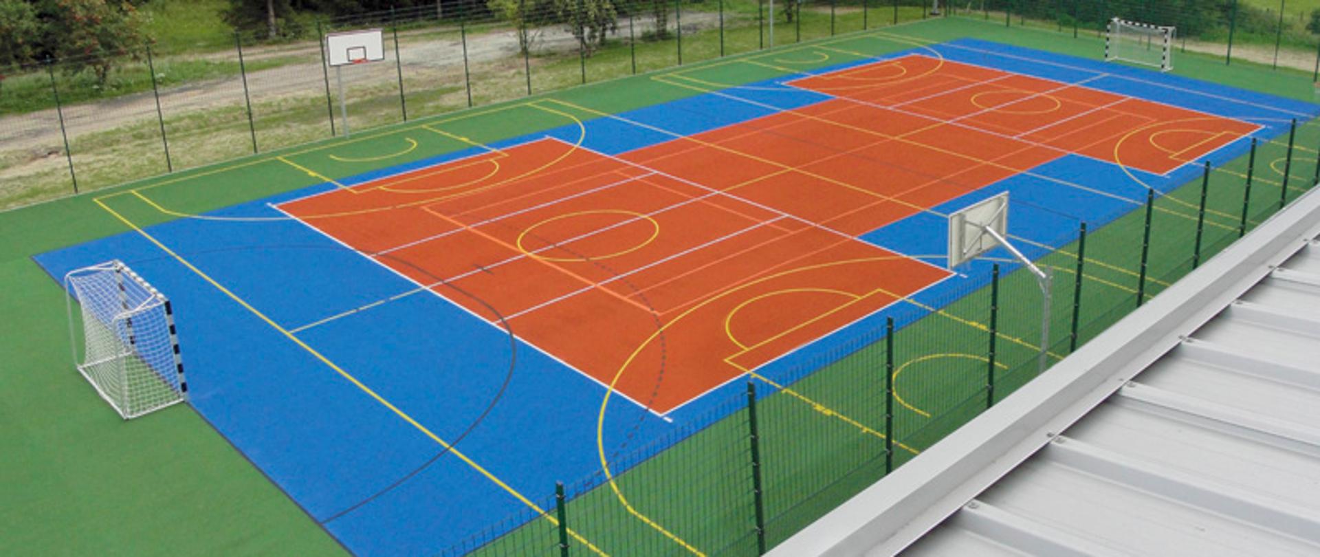 boisko typu Orlik o sztucznej zielono-niebiesko-pomarańczowej nawierzchni z bramkami do piłki ręcznej i koszami do koszykówki, na boisku żółte i białe linie wyznaczające poszczególne obszary boiska