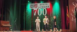 Trzy osoby na scenie z napisem 700 Mesto Dobsina