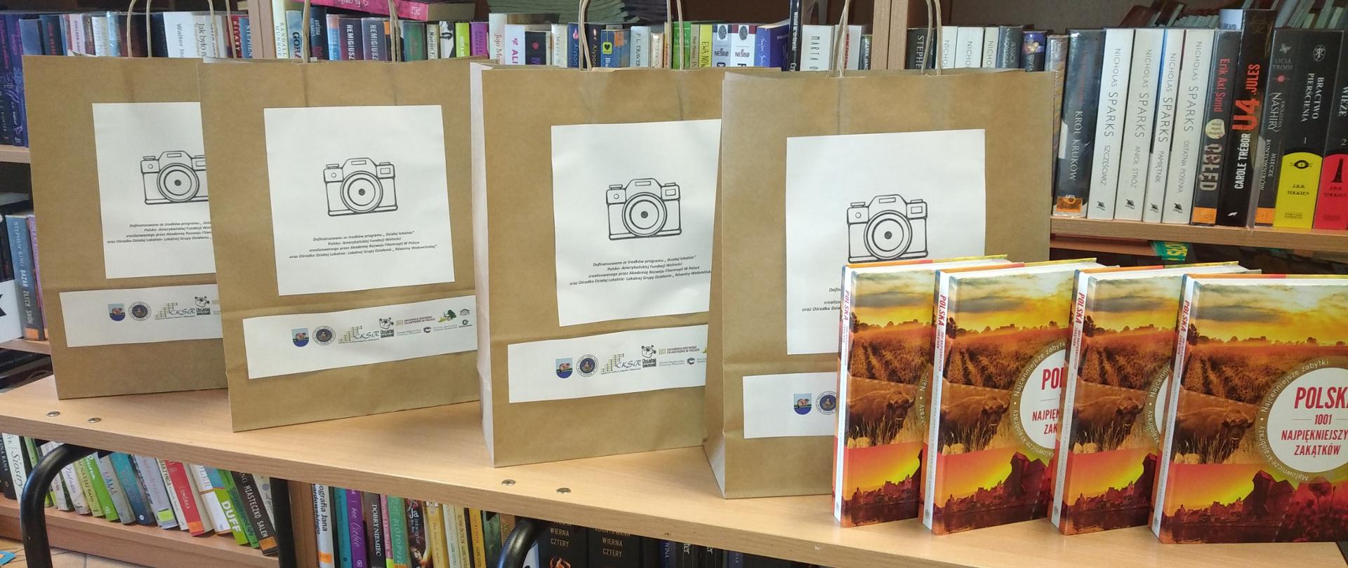 Ustawione na stoliku papierowe torby z obrazem aparatu fotograficznego oraz książki