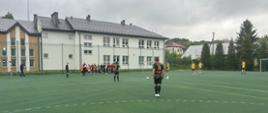 Uczniowie w czarnych strojach ze złotymi numerami na plecach grają na boisku szkoły podstawowej w Łabowej z drużyną przeciwną w pomarańczowych strojach