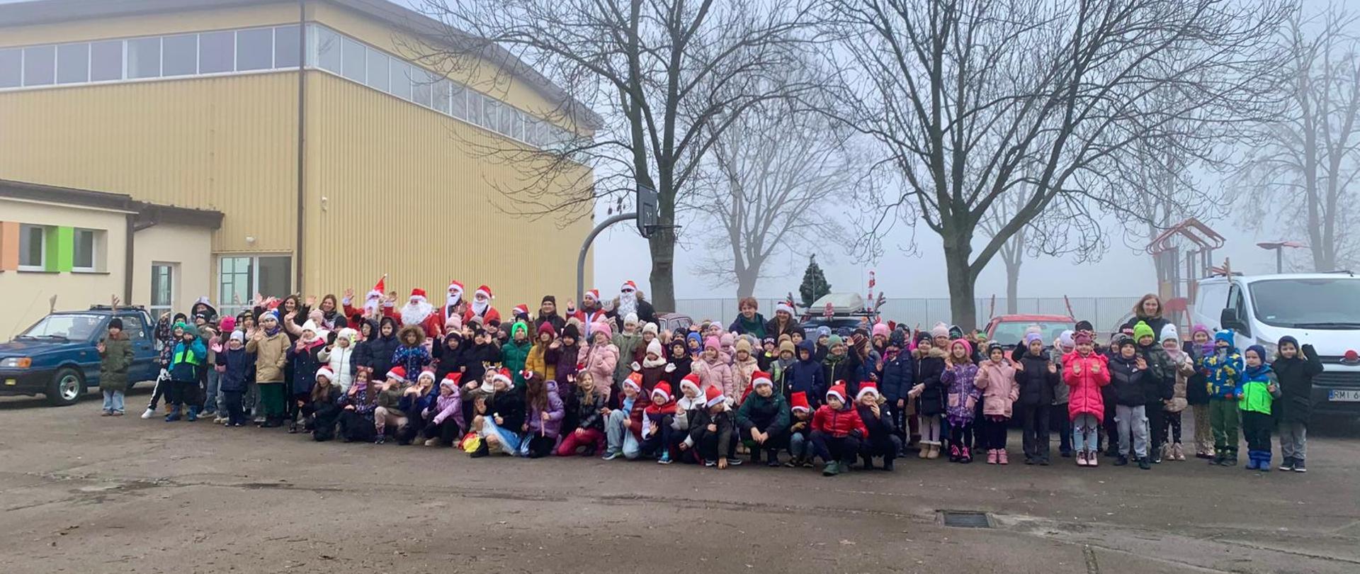 Zdjęcie grupowe uczniów, nauczycieli i Mikołajów na tle zabytkowych samochodów