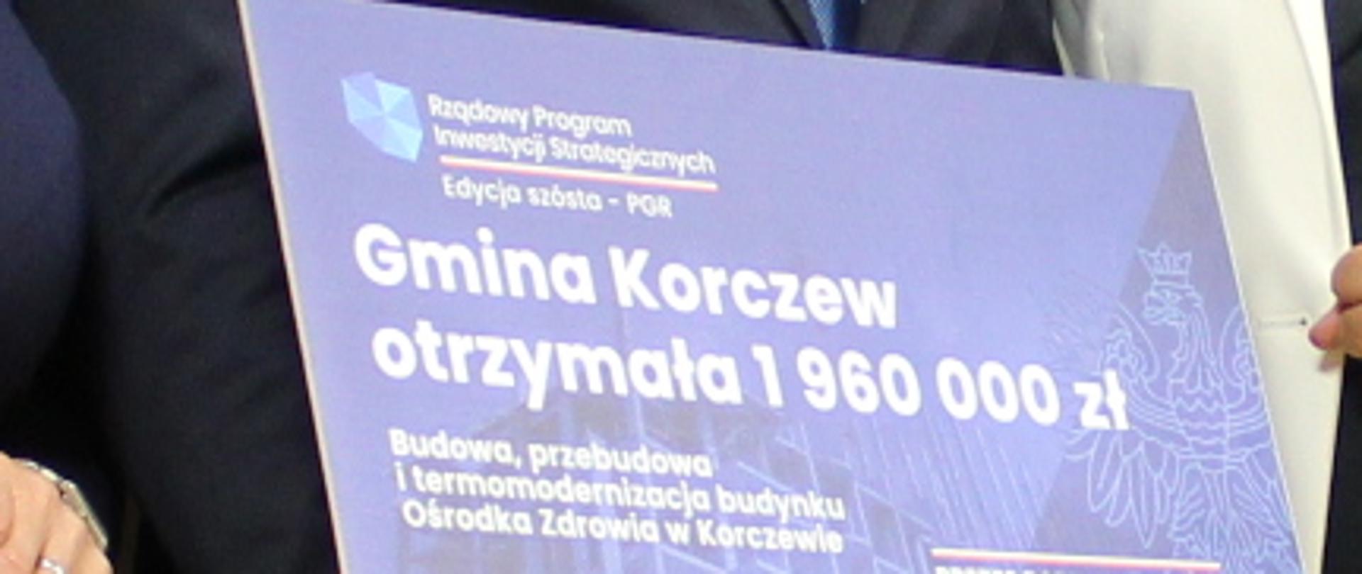 na tle napisu tablicy z napisem "Powiat Siedlecki" stoi osiem osób. Jedna trzyma czek z napisem "Rządowy Program inwestycji strategicznych, edycja szósta PGR. Gmina Korczew otrzymała 1960000 Budowa, przebudowa i termomodernizacja budynku Ośrodka Zdrowia w Korczewie. Prezes Rady Ministrów Mateusz Morawiecki.