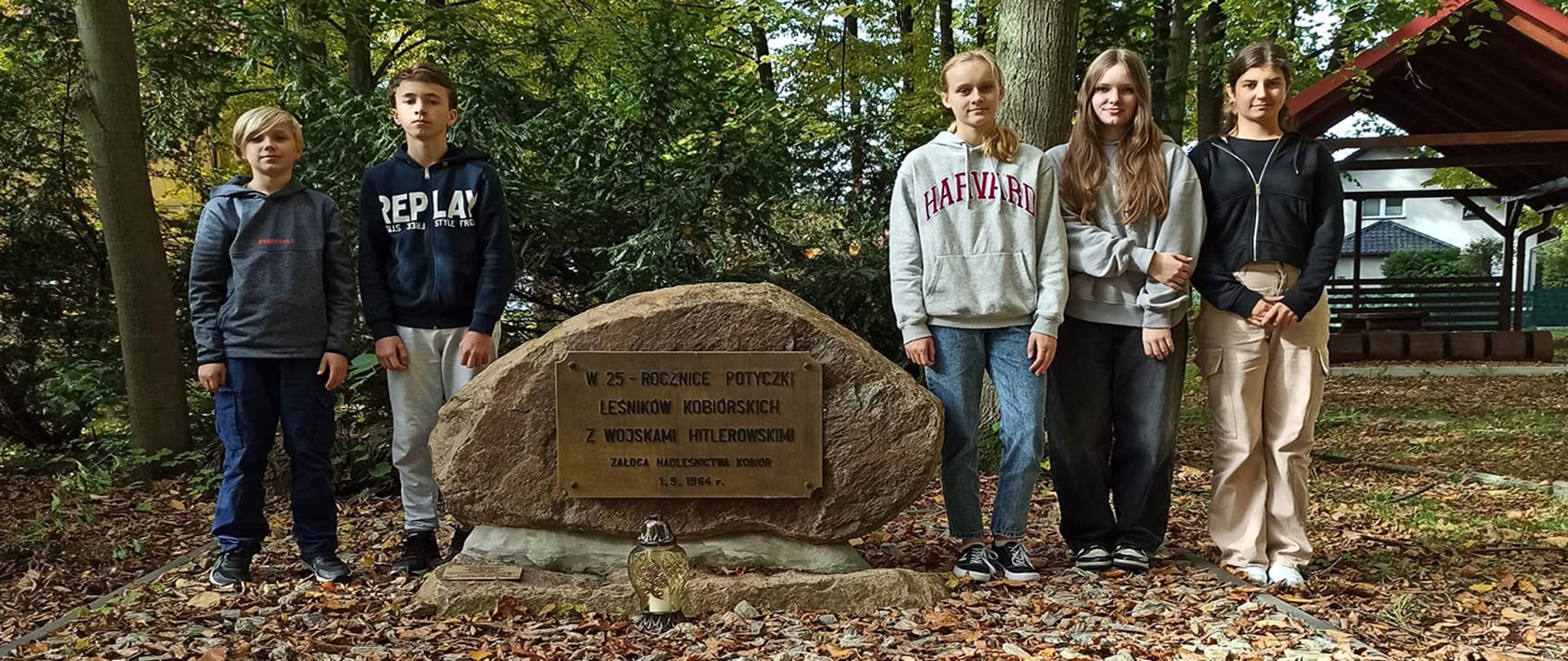 Grupa uczniów stojąca przy głazie upamiętniającym potyczkę leśników z hitlerowcami