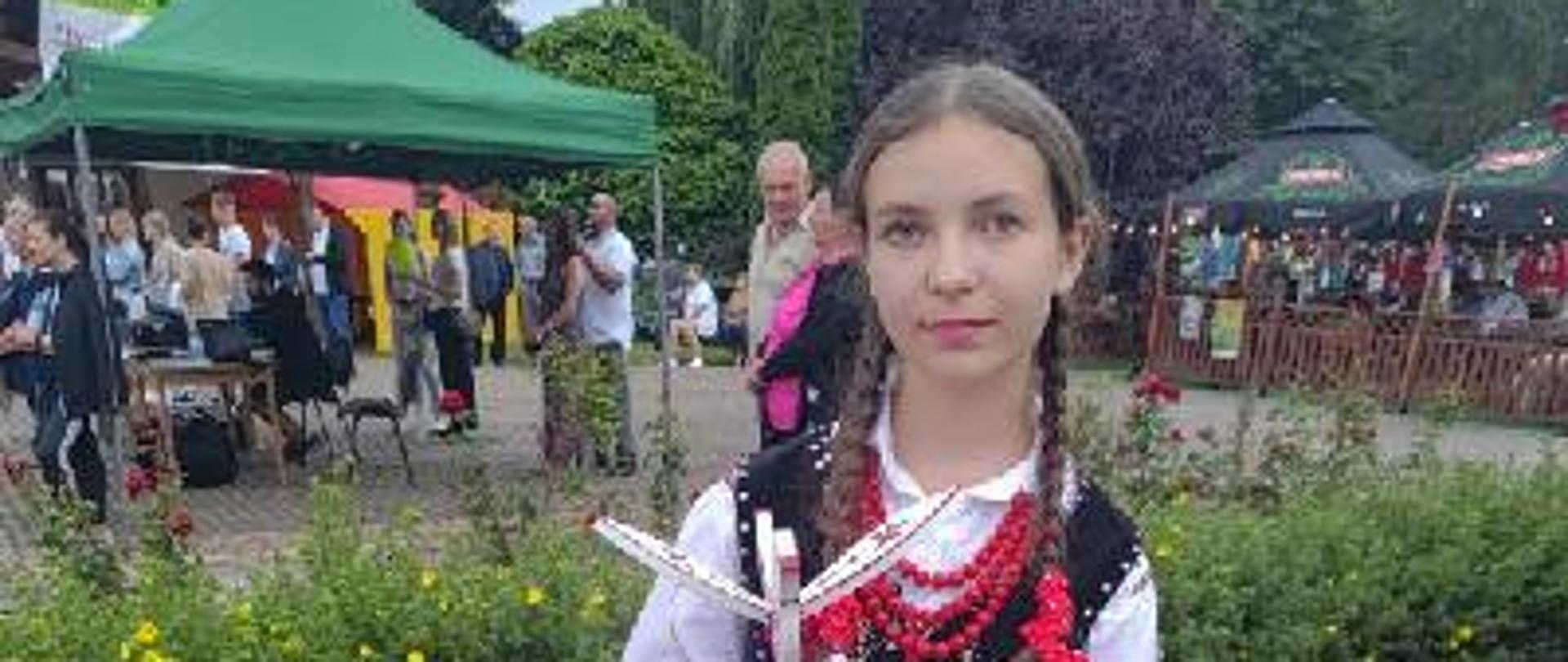 dziewczynka w ludowym stroju pozuje do zdjecia z dyplomami 