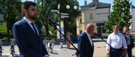 Zdjęcie przedstawia trzy osoby stojące na placu przed mikrofonami.