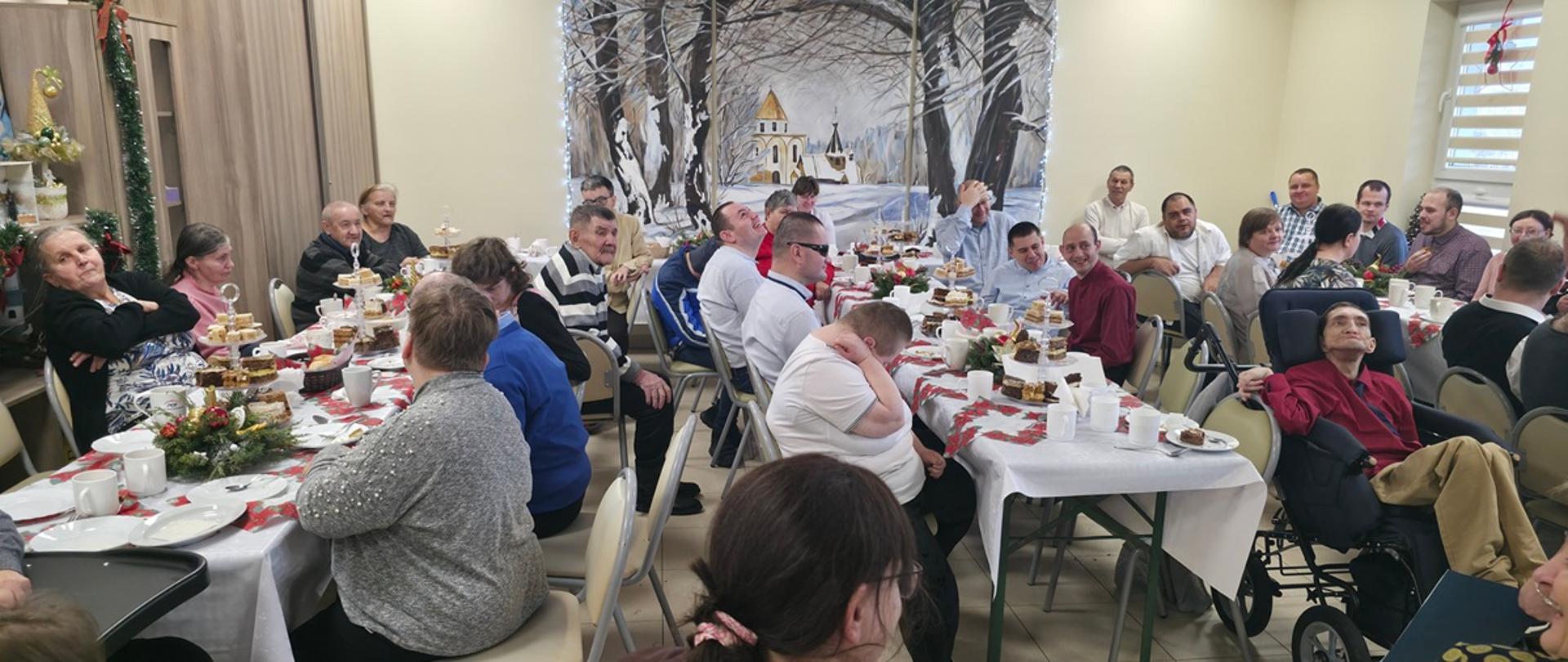mężczyźni i kobiety siedzą wspólnie przy zastawionych jedzeniem stołach 