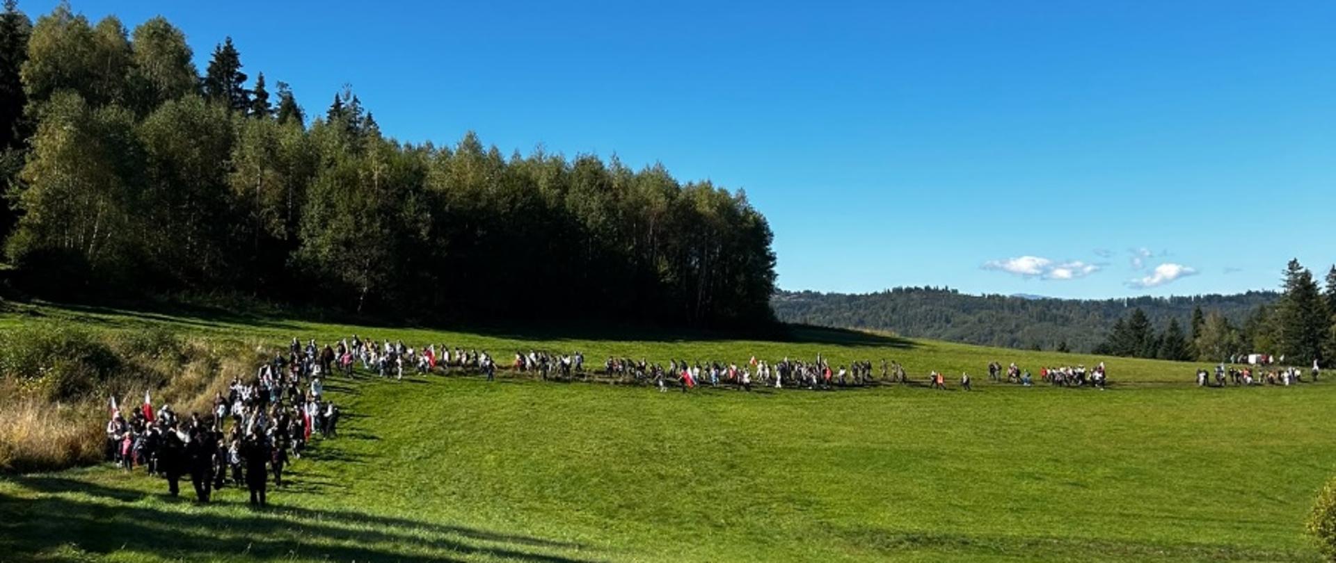 Uczestnicy uroczystości zgromadzeni na leśnej polanie.