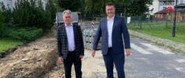 Dwie osoby w garniturach stojące na drodze obok wykopu
