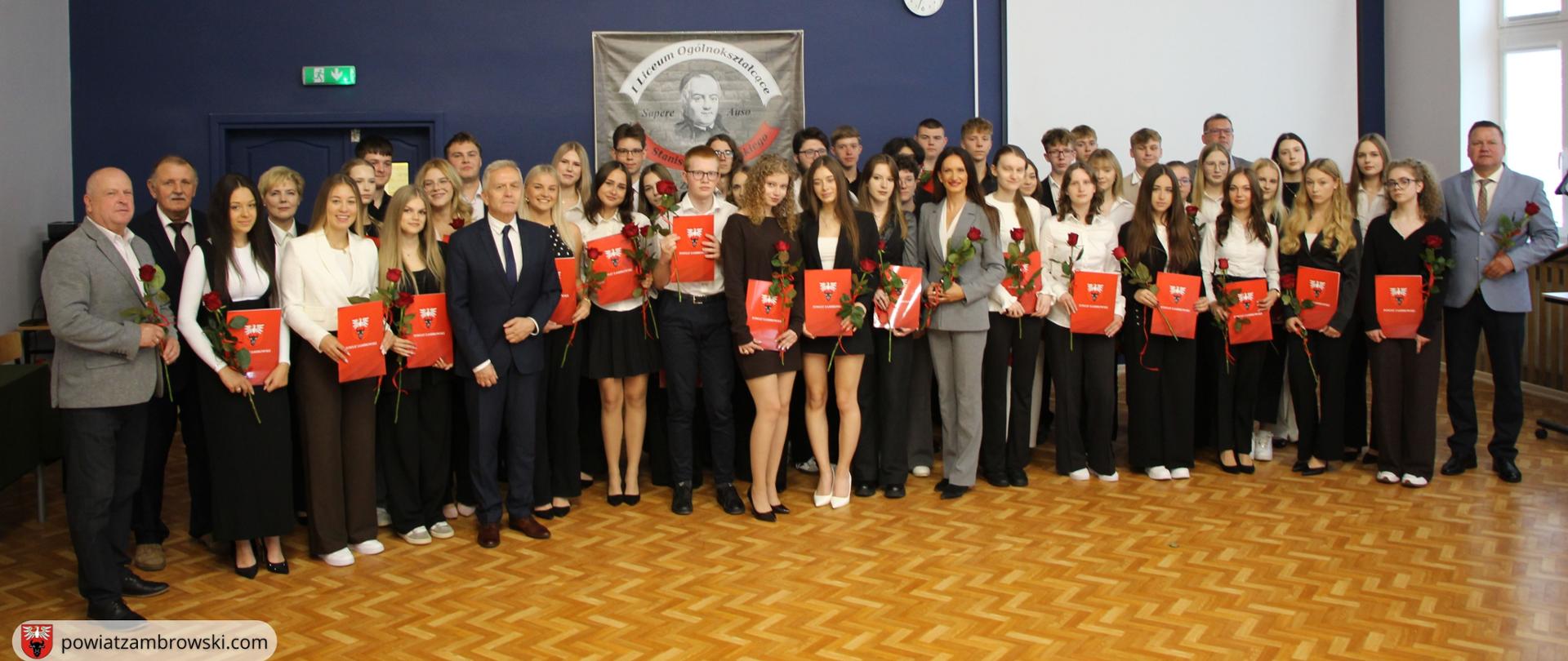 Szeroki kadr dokumentujący całą społeczność stypendystów oraz zaproszonych gości w auli liceum.