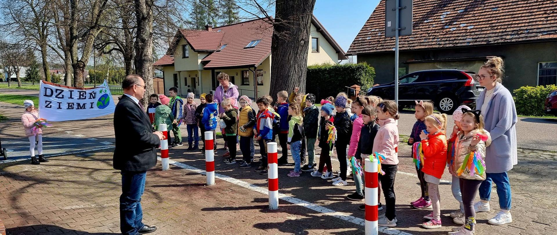 Grupa dzieci z przedszkola z transparentem dzień ziemi oraz wychowawczyniami, naprzeciw grupy stoi sekretarz gminy