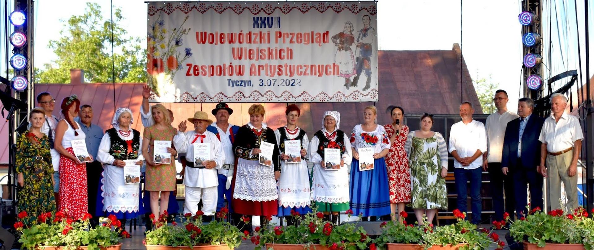 kobiety i mężczyźni stojący na scenie i wspólnie pozujący do zdjęcia, niektórzy ubrani w ludowe stroje 