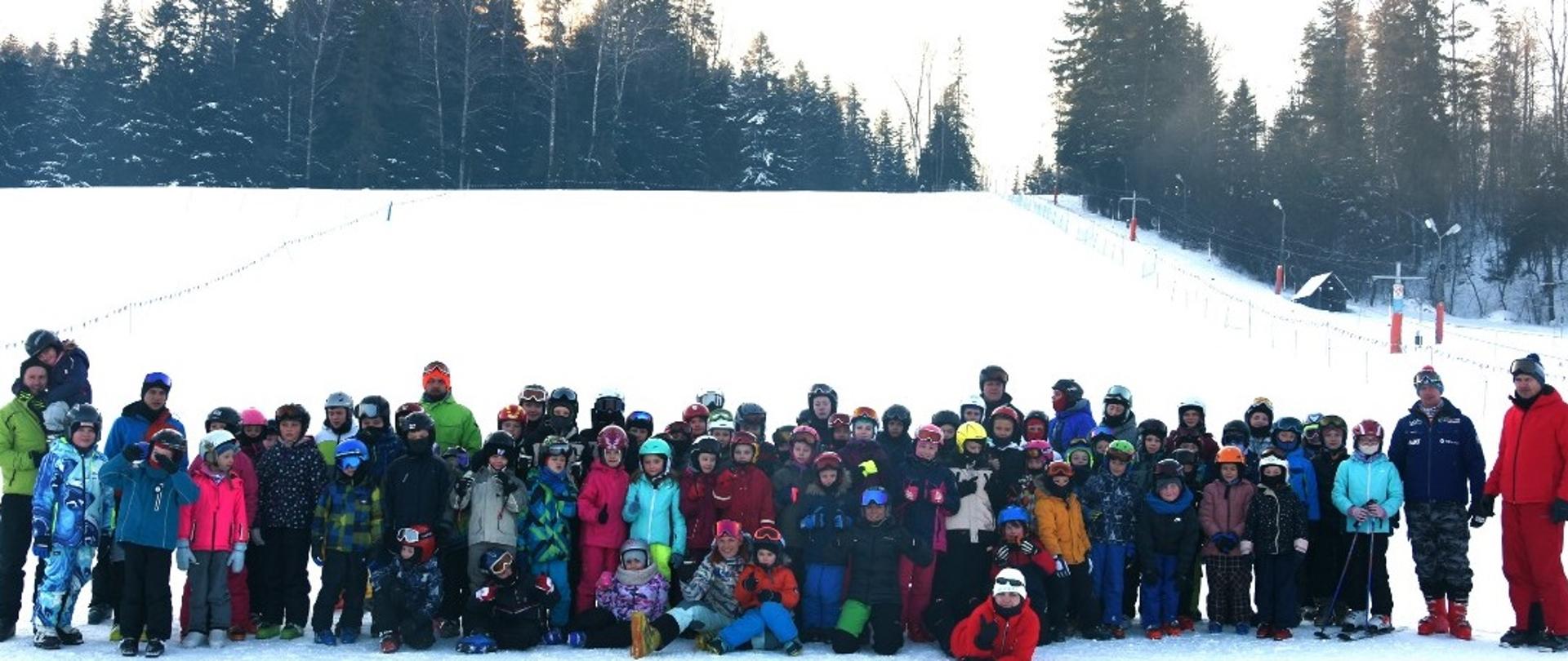 Kilkadziesiąt dzieci w strojach narciarskich stojące na stoku narciarskim
