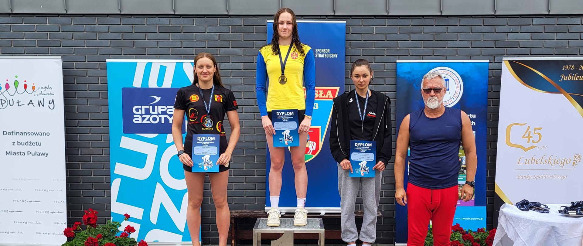 Maja Ryfka na pierwszym stopniu podium. Po prawej stronie podium stoi trener UKP "Fali" Kraśnik Grzegorz Mazurek