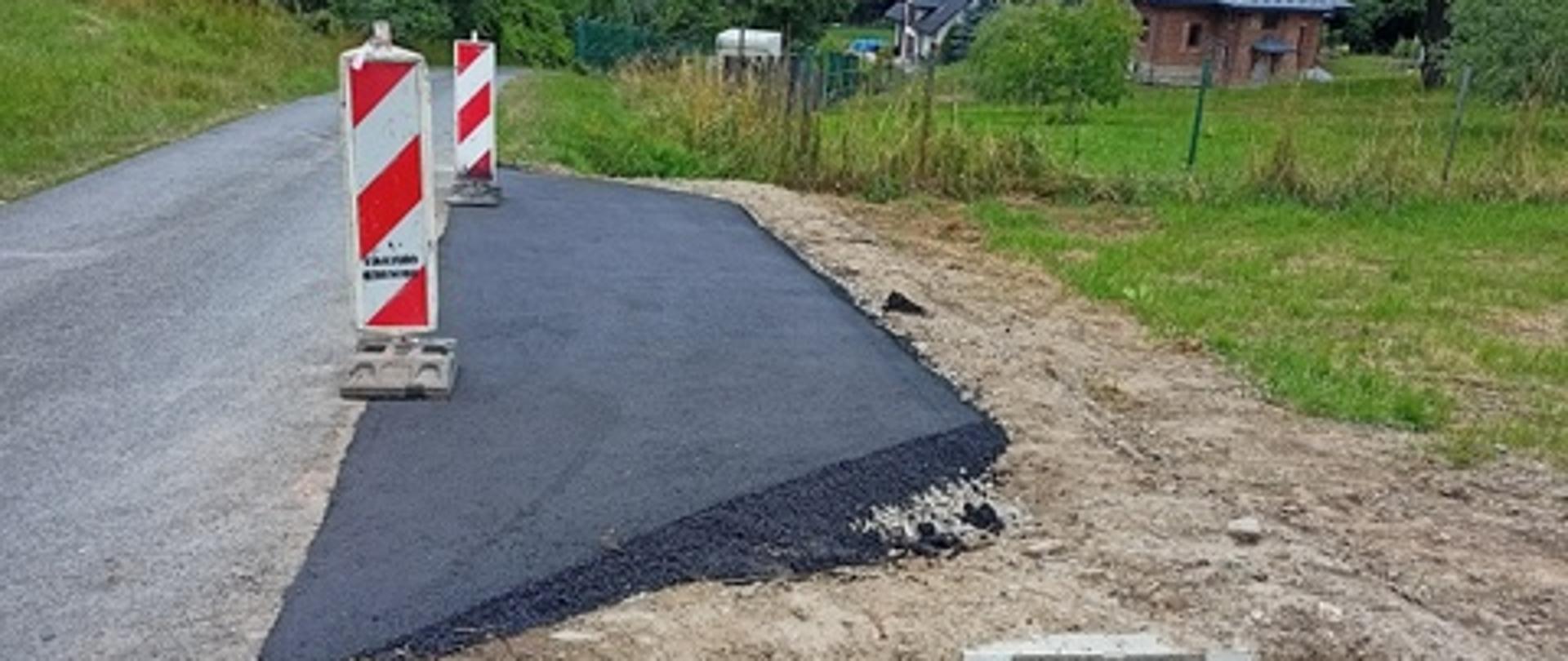 widoczna zatoka asfaltowa łąka na dalszym planie zabudowania