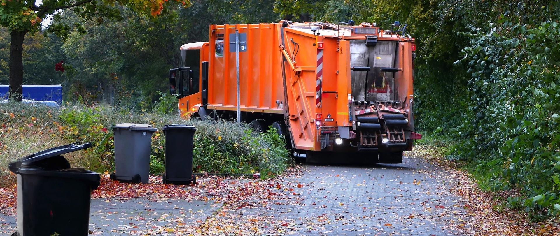 Pomarańczowa śmieciarka odbiera śmieci z osiedla 
