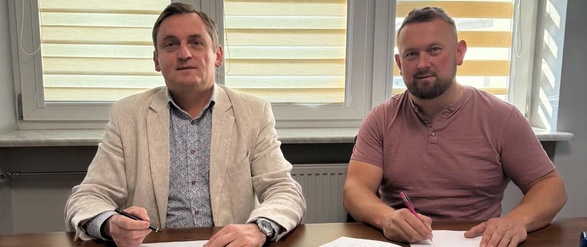 Dwóch mężczyzn w średnim wieku siedzą przy stole i podpisują dokumenty