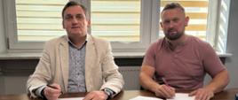 Dwóch mężczyzn w średnim wieku siedzą przy stole i podpisują dokumenty