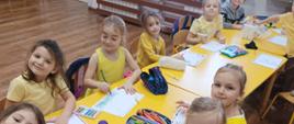 Ubrane na żółto dzieci z oddziału przedszkolnego siedzą przy żółtych stolikach i piszą listy