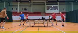 Podczas gry w tenisa - uczestnicy stoją przy stołach, rozgrywają mecz