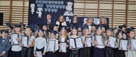 Pierwszoklasiści z dyplomami w odświętnych strojach. Za uczniami stoją Wójt Gminy Mielec, Dyrekcja Zespołu Szkół w Chorzelowie i wychowawcy klas pierwszych.