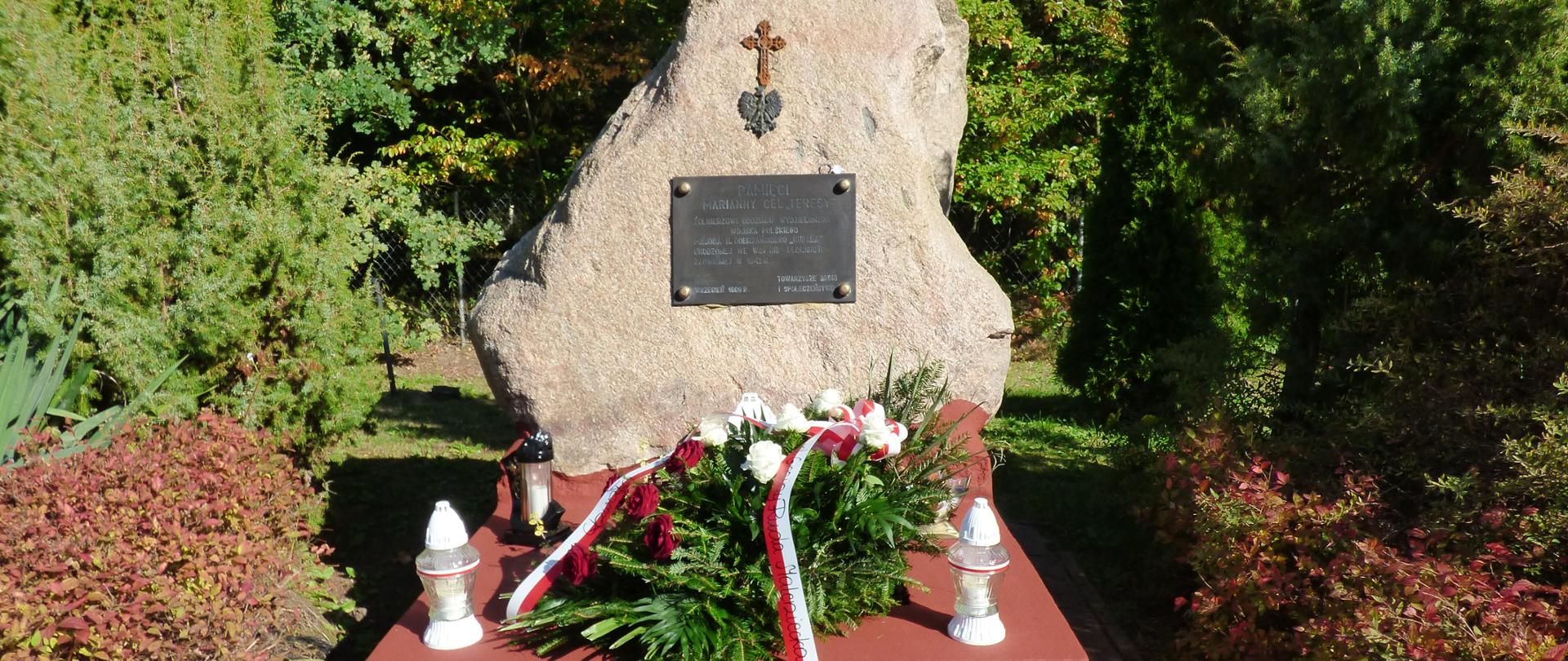 Zdjęcie ukazuje pomnik poświęcony pamięci Marianny Cel „Teresy”
– Żołnierzowi Oddziału Wydzielonego Wojska Polskiego Majora H. Dobrzańskiego „Hubala” wraz ze złożonymi kwiatami w barwach patriotycznych i zapalonymi zniczami.
