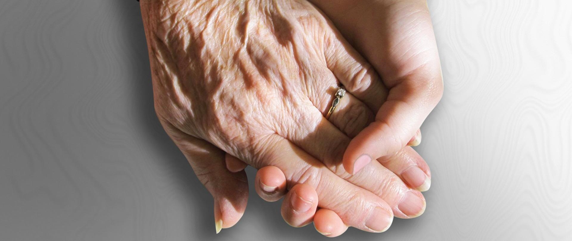zdjęcie dwóch dłoni, dłoń młodszej osoby trzyma dłoń starszej osoby