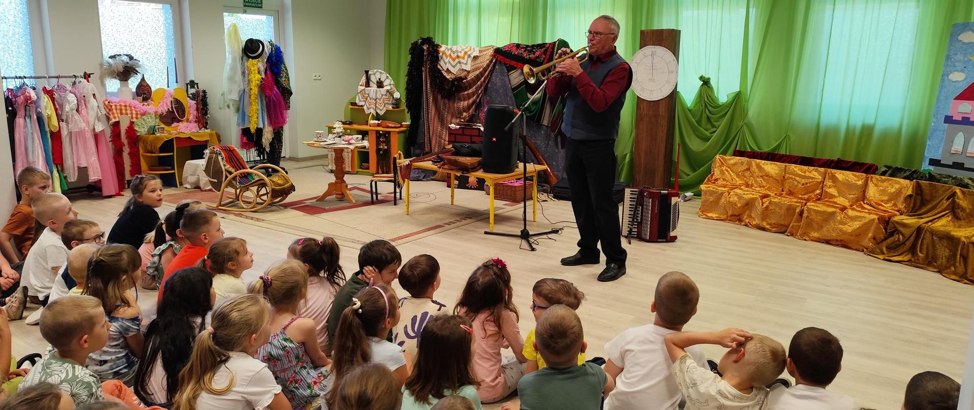 Pan gra na trąbce, dzieci słuchają 