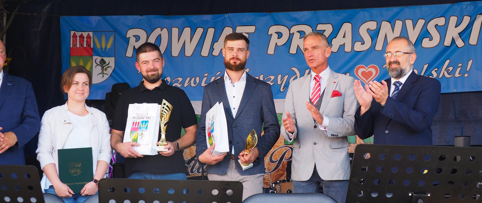 Wręczenie nagród dla najlepszych rolników w powiecie przasnyskim. Na scenie dożynkowej stoją samorządowcy Starosta Przasnyski, Wójt Gminy Krzynowłoga Mała Jerzy Humięcki, Senator Jan Maria Jackowski wraz z nagrodzonymi rolnikami z terenu gminy Krzynowłoga Mała.