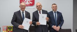 trzej mężczyźni w garniturach podpisują dokumenty przy stole