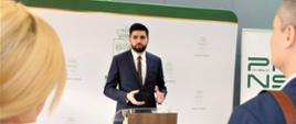 Zdjęcie przedstawia jedną osobę stojącą wewnątrz budynku przy mównicy
