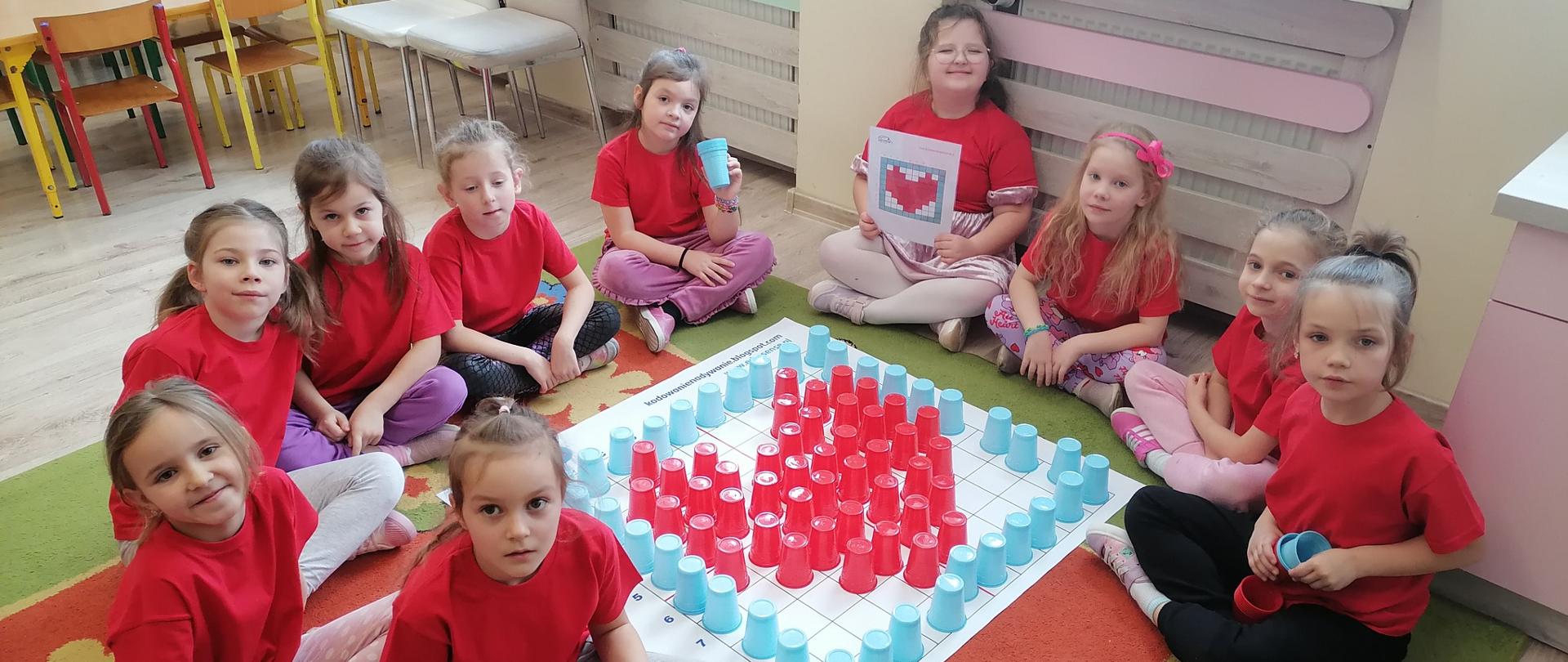 10 Dziewczynek w czerwonych koszulkach siedzą na dywanie