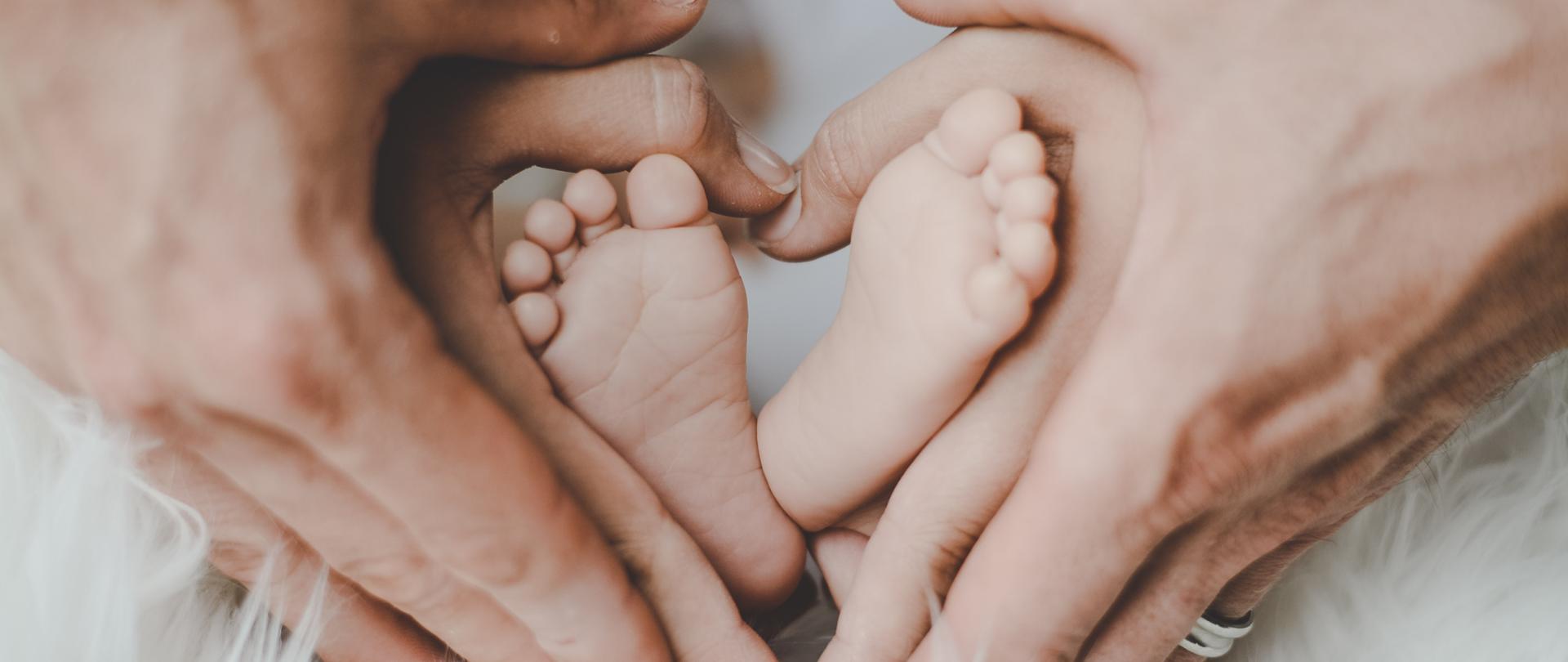 rodzice trzymający stopy noworodka, dłonie ułożone w kształt serca, na dole zdjęcia białe futro