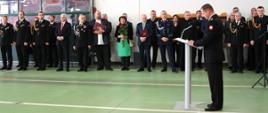 Fotografia grupowa - przedstawia przedstawicieli Senatu, samorządów, służb mundurowych, kapelana oraz przedsiębiorców. Zaproszeni goście słuchają przemówienia komendanta PSP w Sokołowie Podlaskim, który stoi przy mównicy.
Zdjęcie wykonane w garażu PSP w Sokołowie podczas uroczystego pożegnania komendanta.