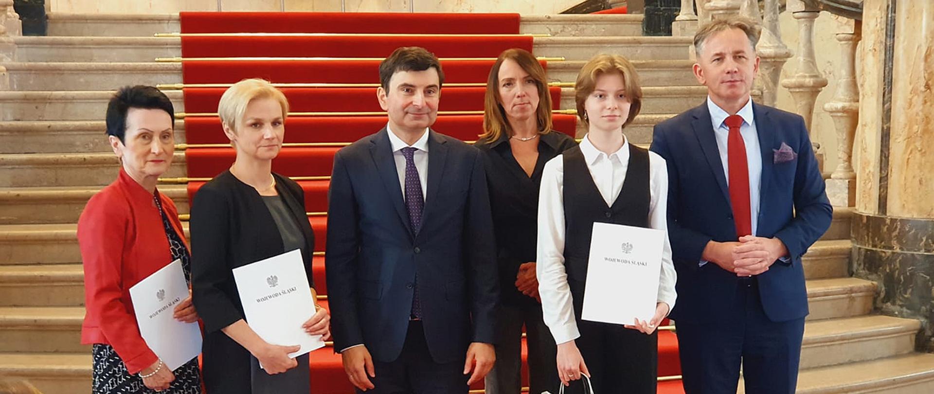 Grupa osób stojąca na tle czerwonego dywanu rozwiniętego na schodach