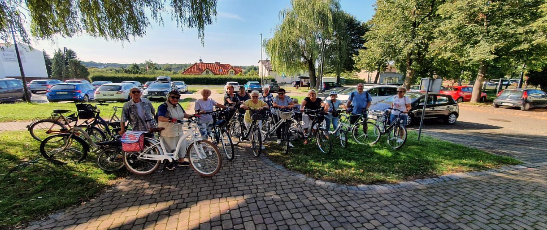 Grupa seniorów z rowerami na parkingu samochodowym