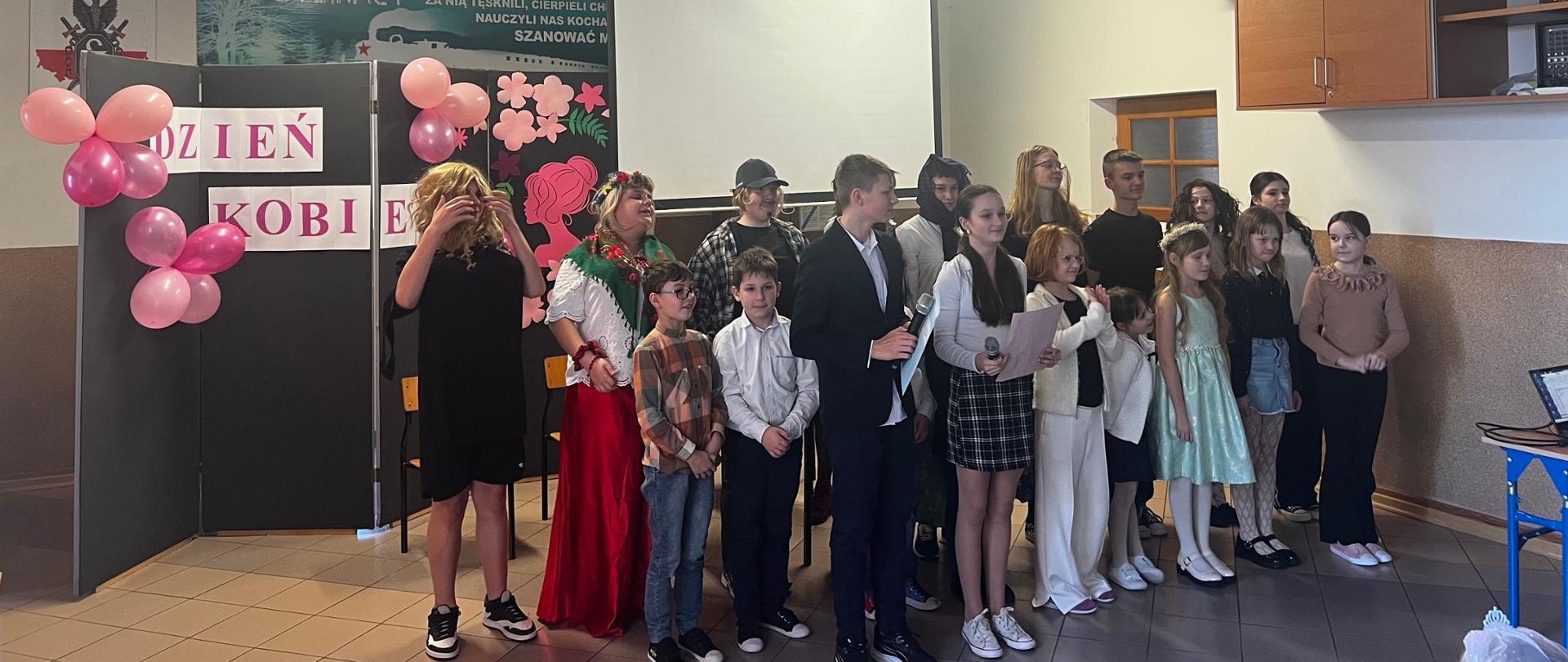 Na scenie stoją wszyscy uczniowie, którzy brali udział w przedstawieniu. Uczniowie są ubrani w odświętnie stroje.