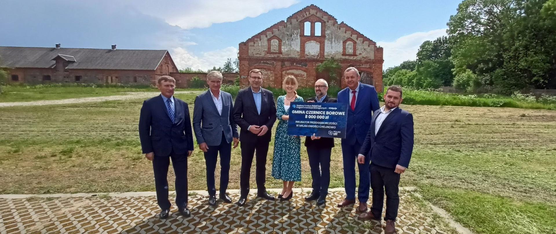 Minister Maciej Małecki, wręczył promesę przedstawicielom Gminy Czernice Borowe. Na zdjęciu samorządowcy z ministrem, w tle zabudowania podworskie w Chojnowie.