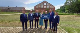 Minister Maciej Małecki, wręczył promesę przedstawicielom Gminy Czernice Borowe. Na zdjęciu samorządowcy z ministrem, w tle zabudowania podworskie w Chojnowie.