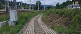 Droga o nawierzchni z płyt betonowych, w tle trakcja kolei.