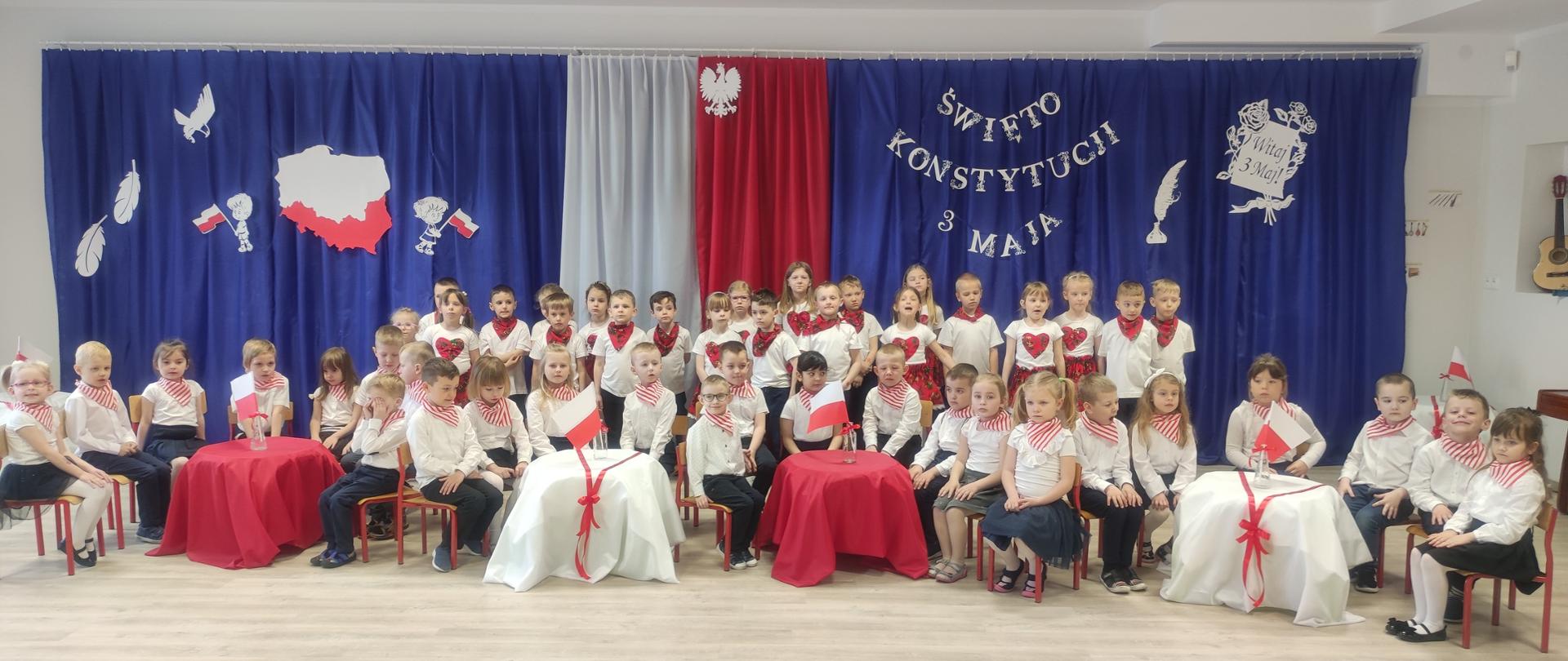 Dzieci w galowych strojach na tle napisu ŚWIĘTO KONSTYTUCJI 3 MAJA