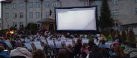 Ludzie siedzący na leżakach, oglądają film na dużym ekranie na placu przed dużym budynkiem